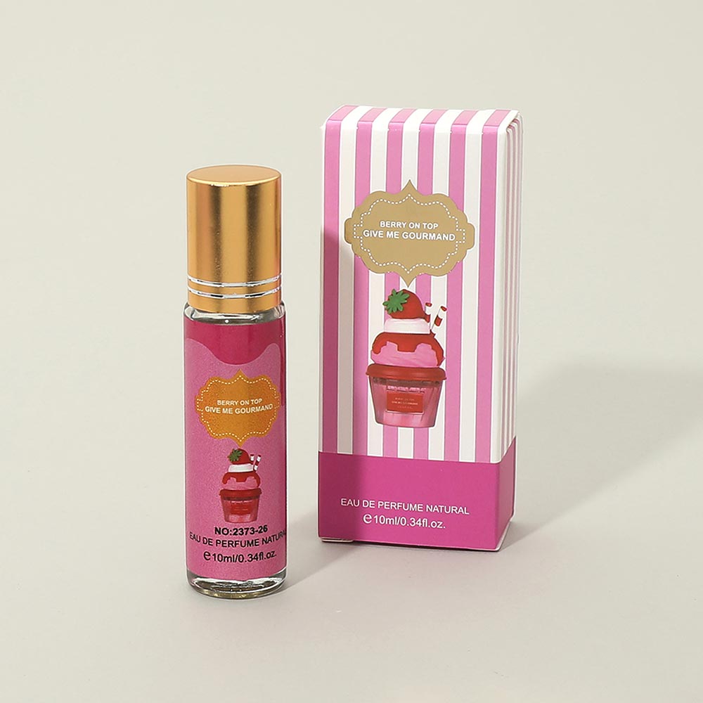 10ml mini eau de parfum roll-on bottle with gold cap and pink "Berry on Top Give Me Gourmand" label featuring strawberry sundae illustration, next to matching pink and white striped gift box, warm gray background