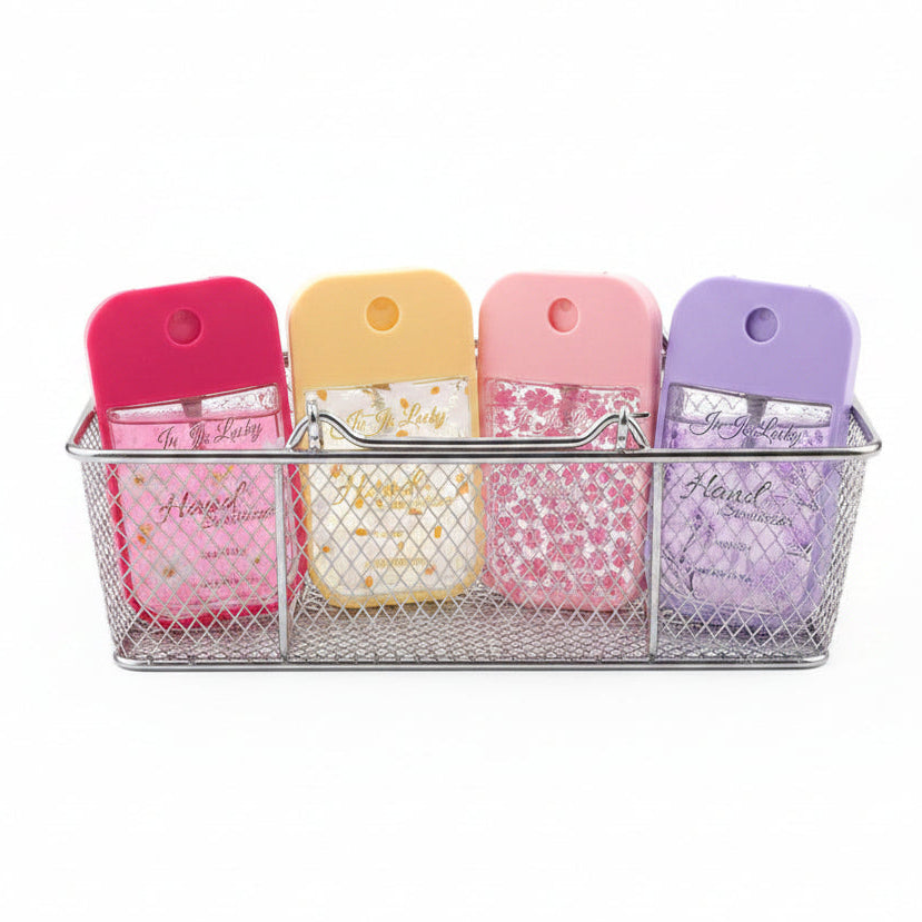 Four Ju Ju Lucky floral pocket hand sanitizer spray bottles in hot pink Camellia, yellow Daisy, light pink Rose, and lavender Lavender scents displayed upright in a silver wire mesh basket, white background