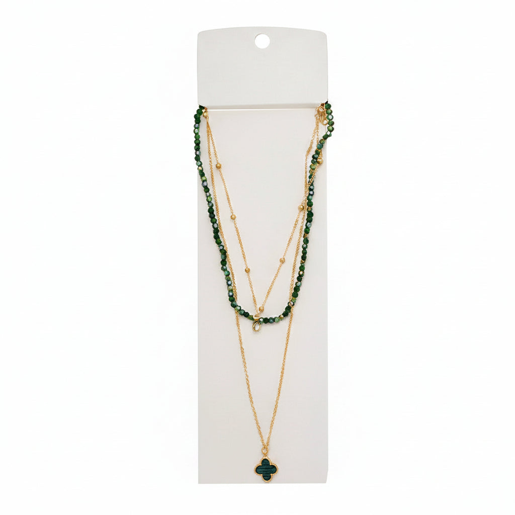 Green faceted crystal beaded layered necklace with gold satellite chain and dark green quatrefoil clover pendant on white display card, white background