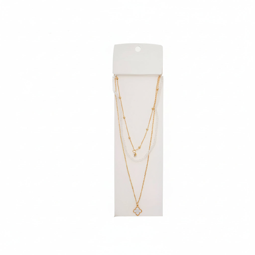 Crystal clear beaded layered necklace with gold satellite chain and open-frame gold quatrefoil clover pendant on white display card, white background