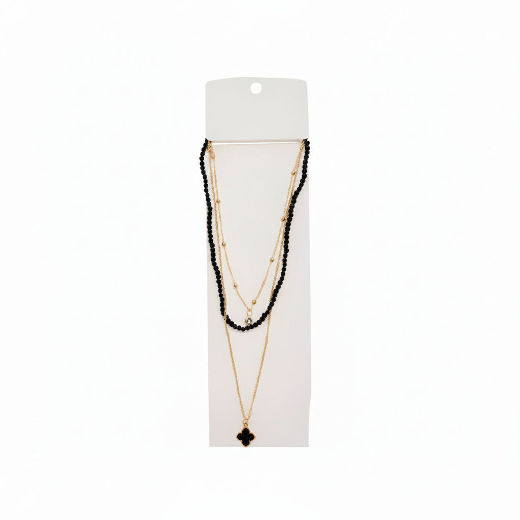 Black faceted crystal beaded layered necklace with gold satellite chain and black quatrefoil clover pendant on white display card, white background