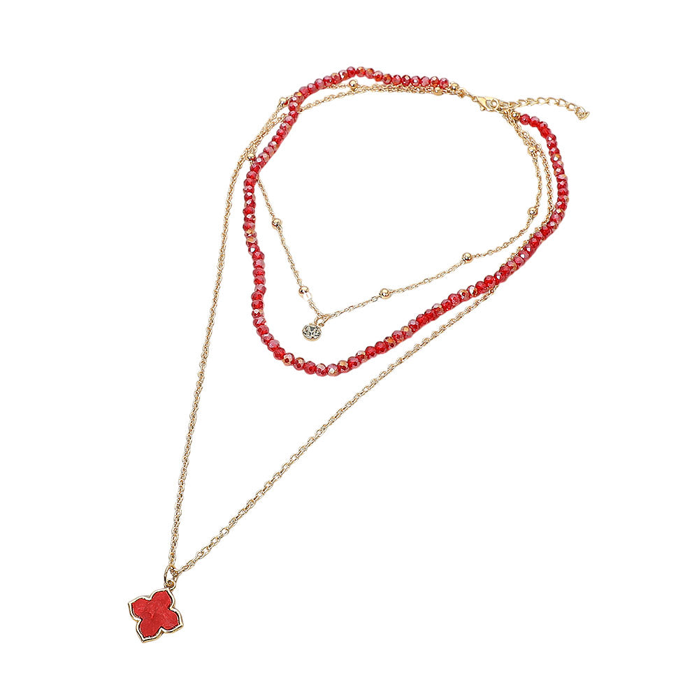 Red faceted crystal beaded layered necklace with gold ball chain and red quatrefoil clover pendant — flat lay on white background showing lobster claw clasp and extender chain