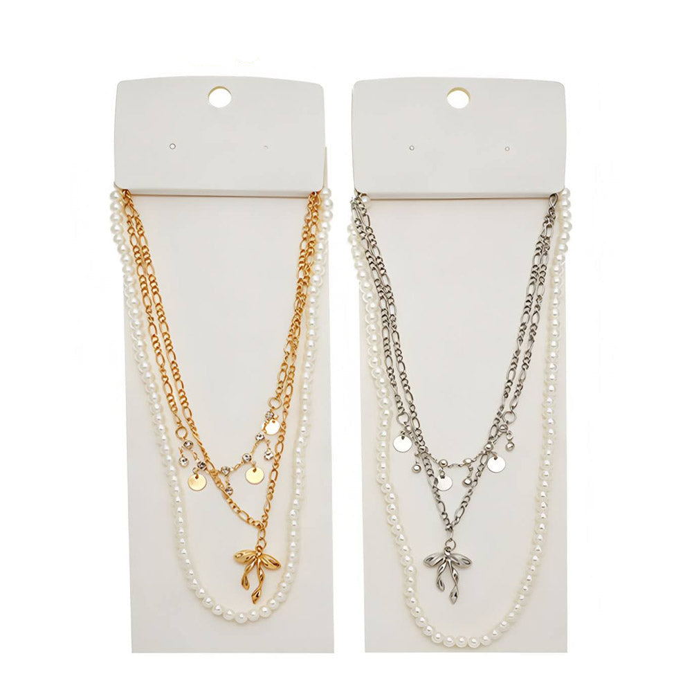 Women's pearl bow pendant layered chain necklace — gold and silver variants side by side on white hang cards showing faux pearl strand, figaro chain with disc charms, and sculptural bow pendant