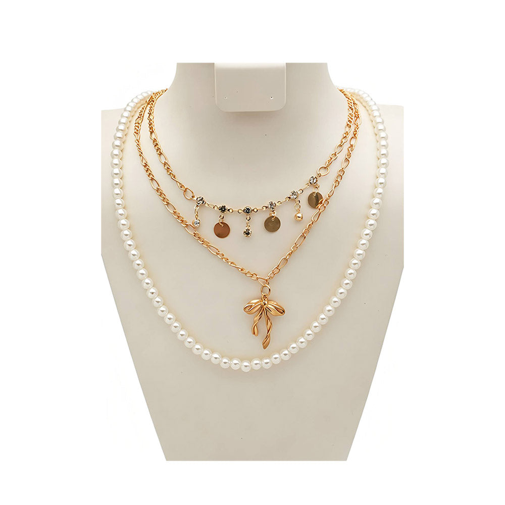 Gold-tone pearl bow pendant layered necklace on white mannequin bust — 3-strand design with faux pearl strand, rhinestone and disc charm chain, and gold figaro chain with sculptural bow pendant