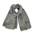 Faded gray camouflage knit scarf loosely looped on a white background, showing its wide shape, charcoal pattern, and pale fringed ends