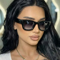 Woman with long black hair wearing glossy black oversized square sunglasses with smoky gradient lenses and paired metallic corner details, styled with a white top and necklace