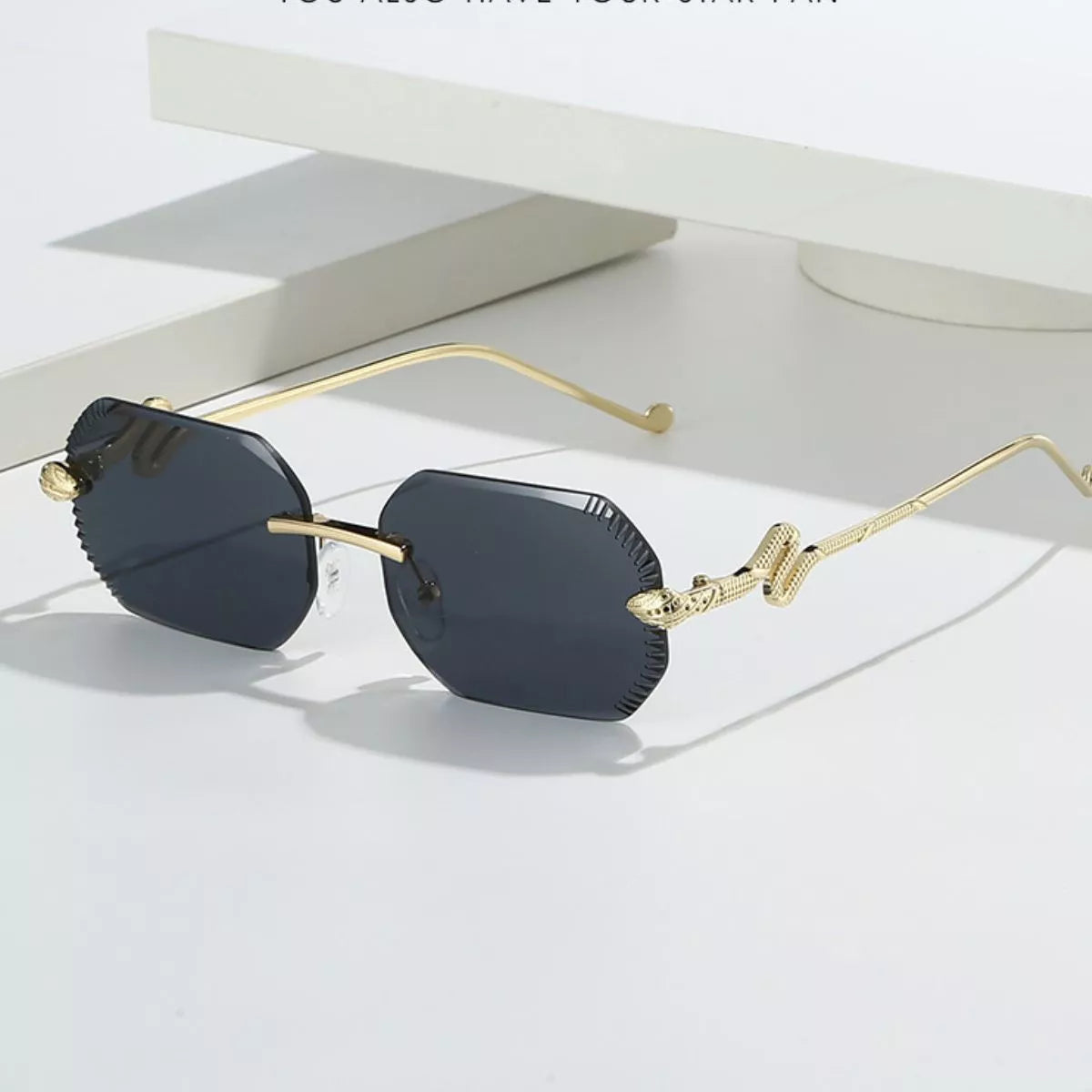 Dark-lens rimless geometric sunglasses with gold-tone snake temples and notched outer lens edges, displayed on a white surface