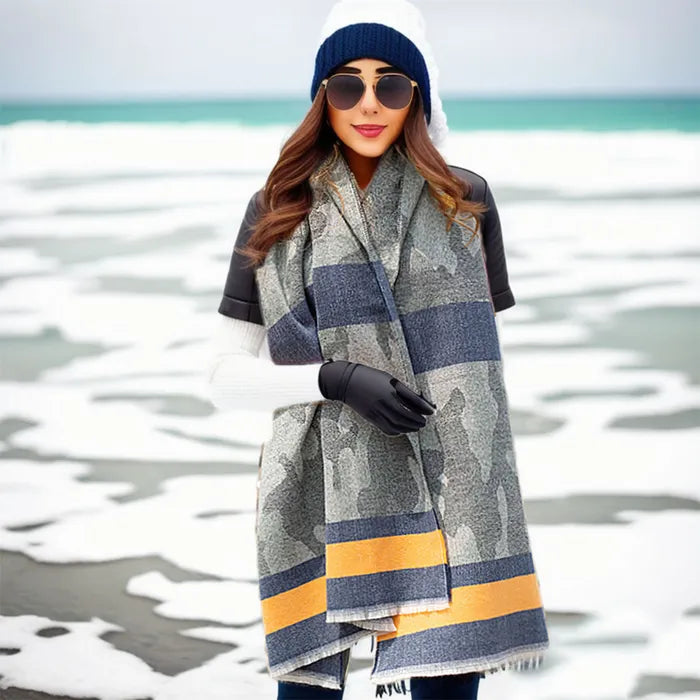 Woman wearing a large plaid scarf with a striped pattern, standing by a body of water.