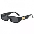Black rectangular sunglasses with dark gray lenses, wide temples, and a textured gold-tone rectangular accent on a white background