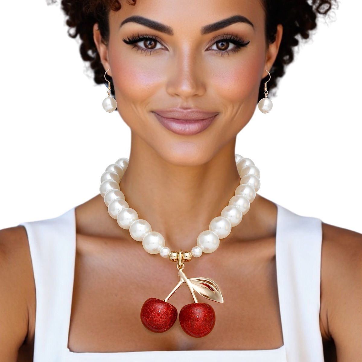 Model wearing a chunky cream faux pearl necklace with a red glitter double-cherry pendant and matching drop earrings, styled with a white square-neck top
