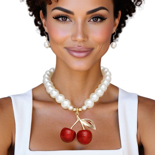 Model wearing a chunky cream faux pearl necklace with a red glitter double-cherry pendant and matching drop earrings, styled with a white square-neck top