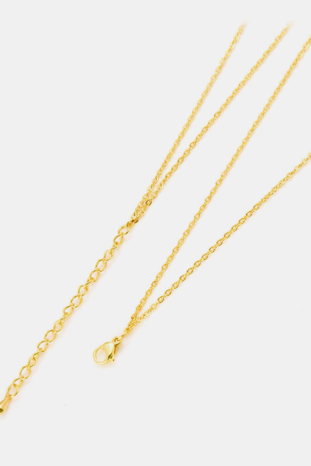Close-up of the necklace’s gold-tone lobster clasp, oval-link extension chain, and delicate chains on a white background