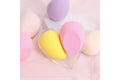 Heart-shaped clear plastic case with yellow and pink makeup beauty blenders surrounded by assorted pastel sponges