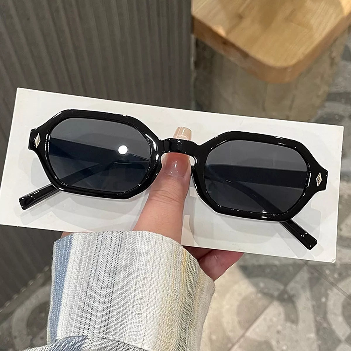 Black geometric sunglasses with dark gray lenses, clipped corners, and silver-tone diamond-shaped accents, shown with open temples on a white surface