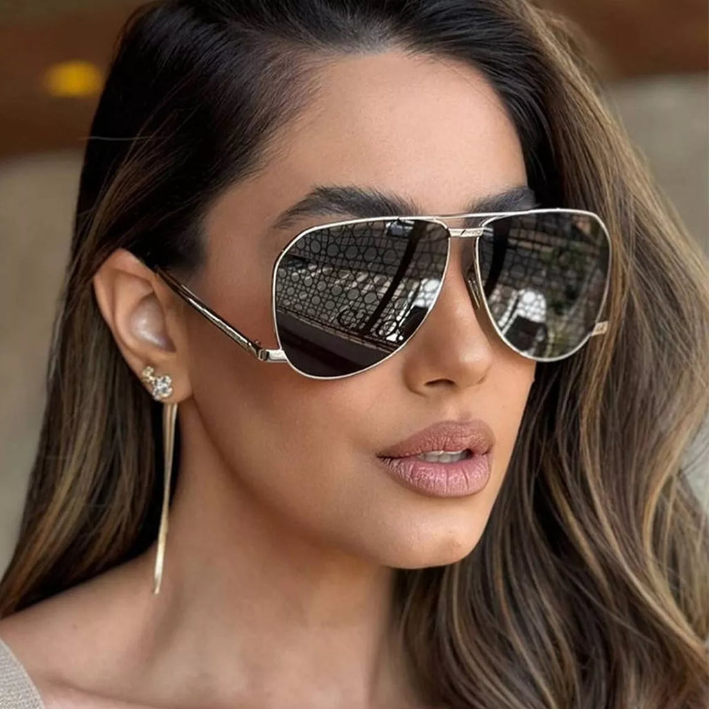 Woman wearing silver-tone aviator sunglasses with dark reflective lenses and a long drop earring, with her brown hair swept to one side