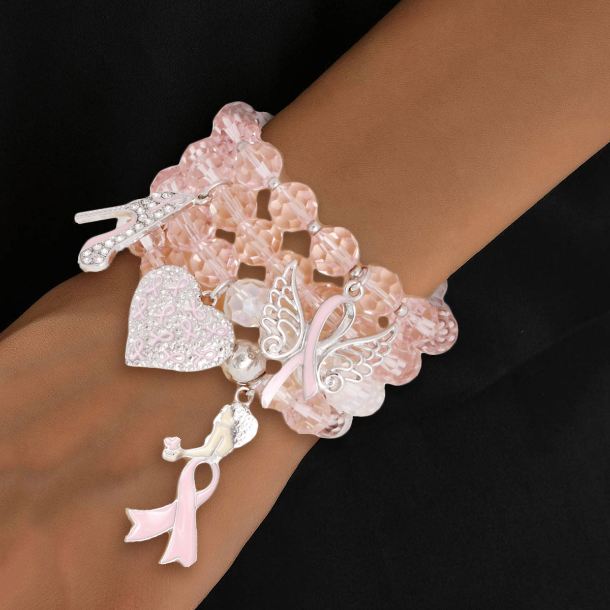 Bracelet with charms including a heart, butterfly, and pink ribbon on a wrist against a black background