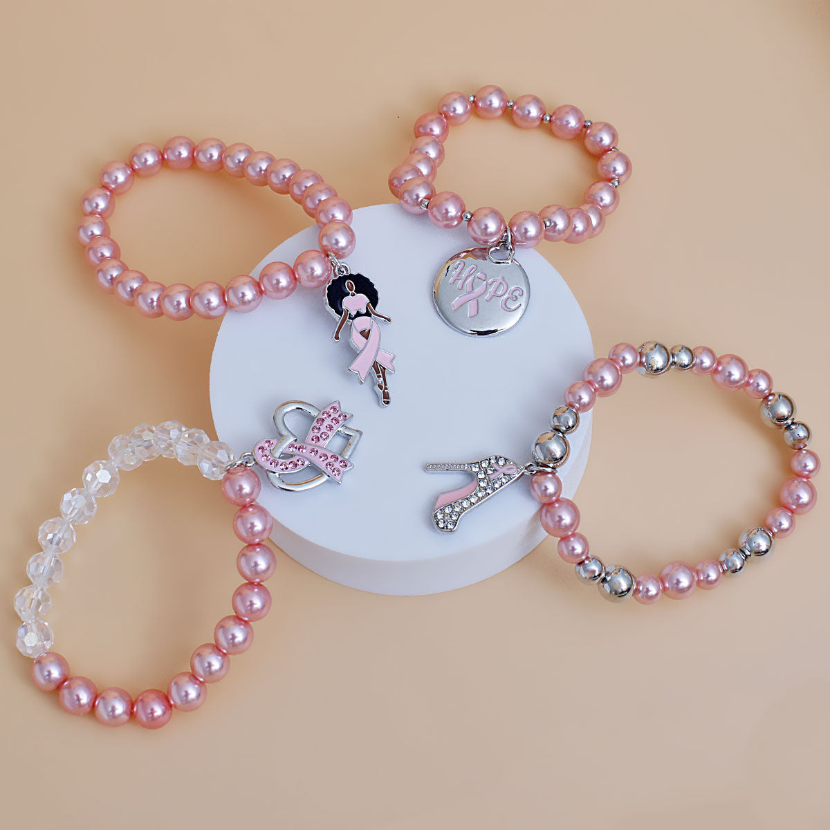 Breast cancer awareness 4-piece light pink pearl stretch bracelet set with Afro woman, Hope disc, pink rhinestone ribbon heart and high heel charms on a white pedestal