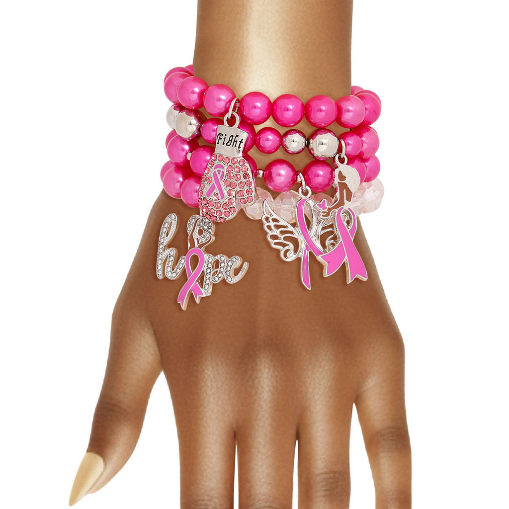 A stack of pink beaded and charm bracelets displayed on a mannequin hand against a white background. The bracelets feature pink pearls, clear beads, a pink awareness ribbon charm, a wing charm, a script 'hope' charm, and a small 'faith' charm.