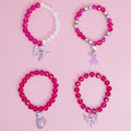 Four fuchsia faceted glass bead stretch bracelets with pink ribbon charms laid out on a pink background, including a fuchsia and clear bead strand and a silver-tone ball bead strand