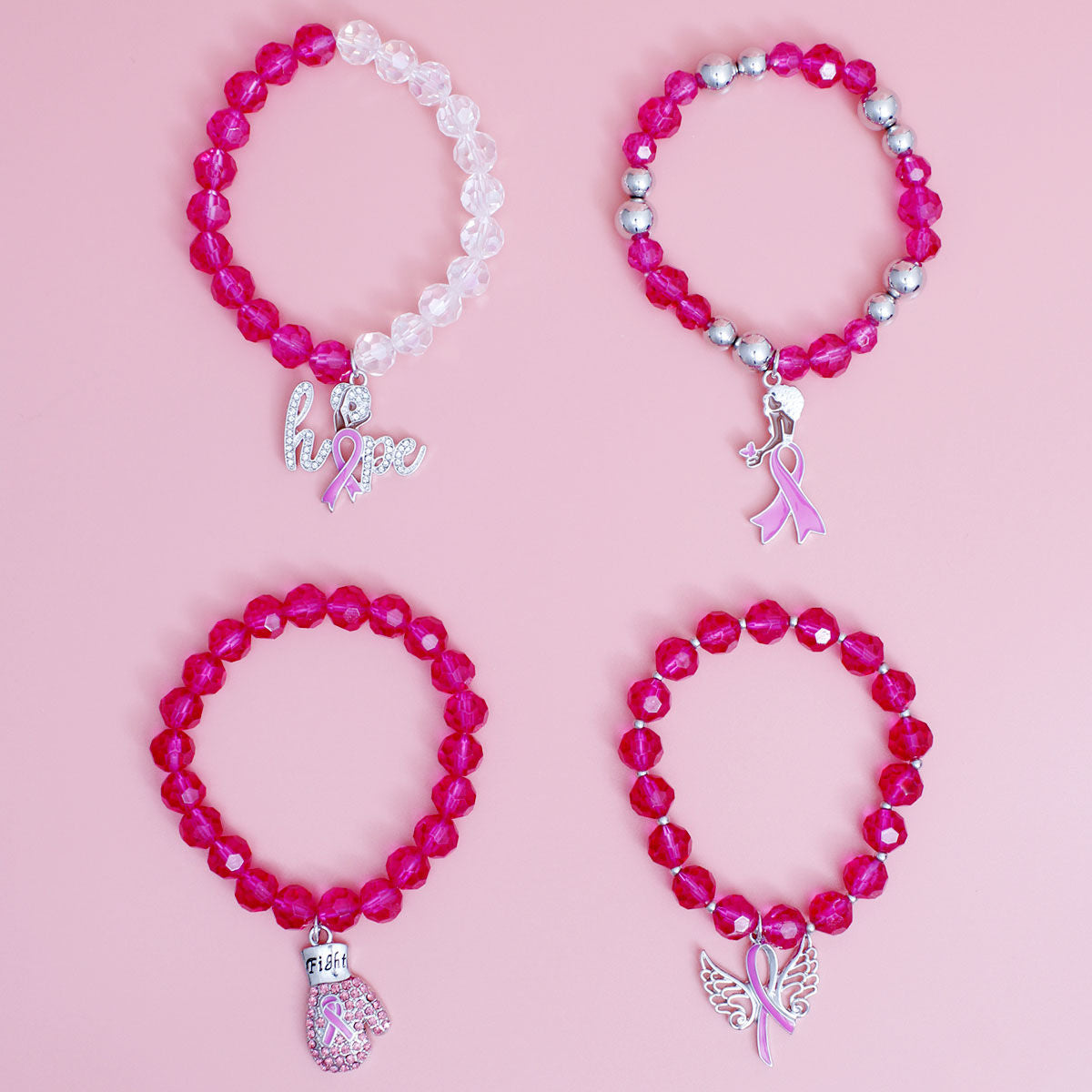 Four fuchsia faceted glass bead stretch bracelets with pink ribbon charms laid out on a pink background, including a fuchsia and clear bead strand and a silver-tone ball bead strand