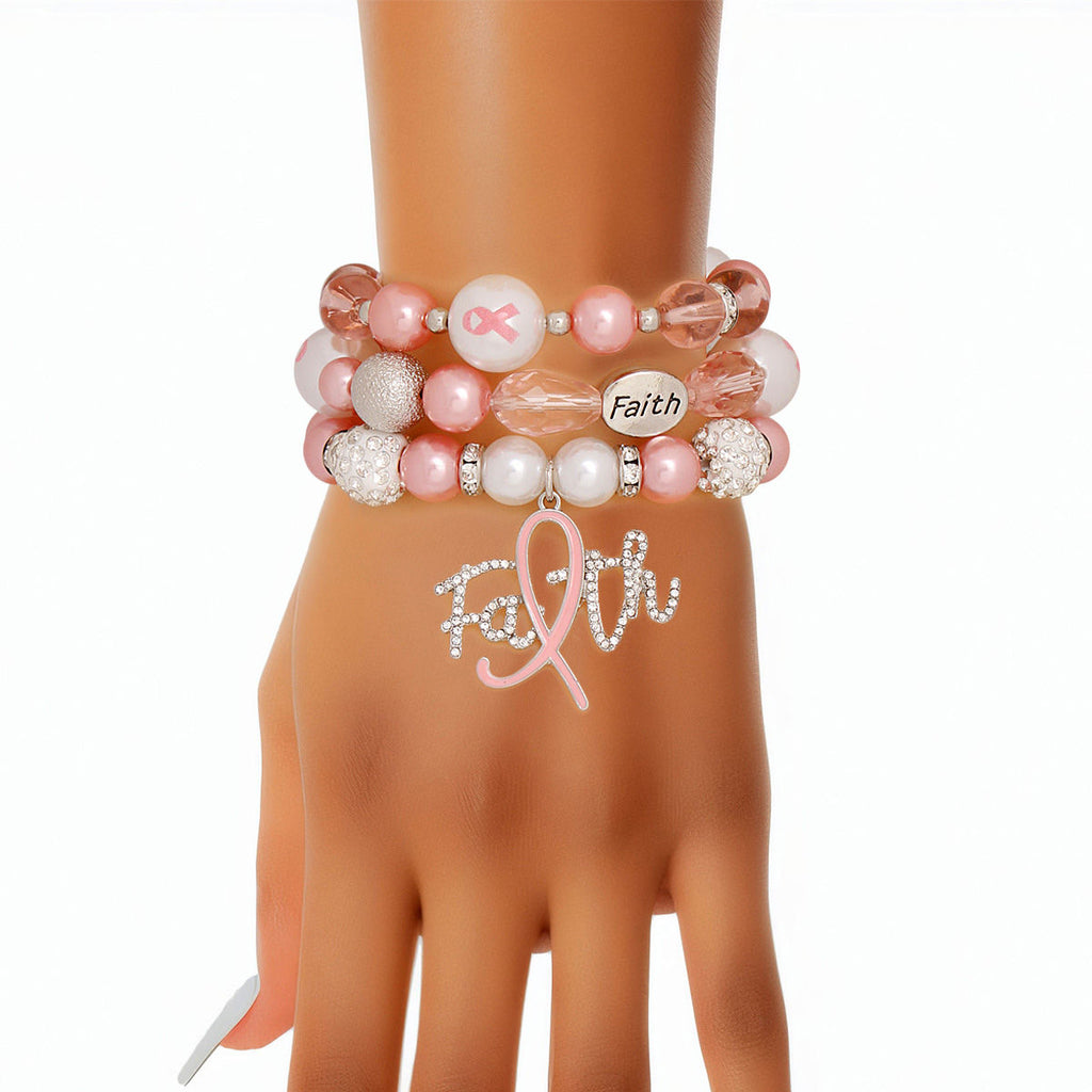 Light pink Faith charm bracelet set stacked on a woman's wrist, showing the rhinestone script Faith charm with pink ribbon "i", white rhinestone pavé beads and engraved Faith bead