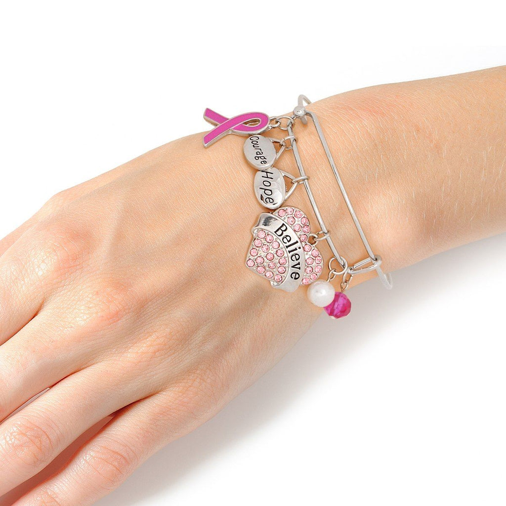 Woman wearing a pink ribbon Believe heart charm bangle on her wrist, showing the pink rhinestone heart, Courage and Hope charms and fuchsia enamel ribbon