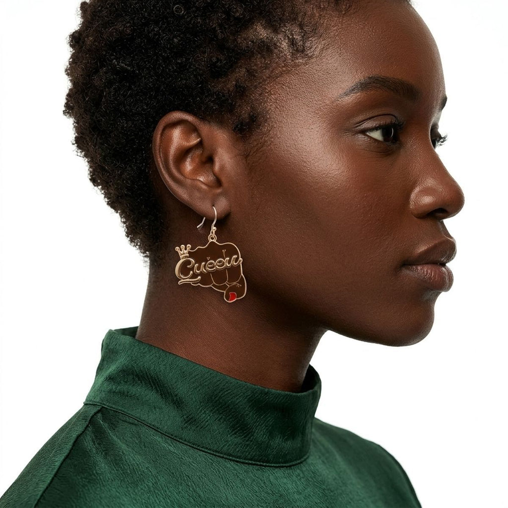 Side profile of Black woman with short natural hair wearing brown epoxy raised fist "Queen" crown dangle earring on gold fish hook wire, shown against white background wearing green satin turtleneck