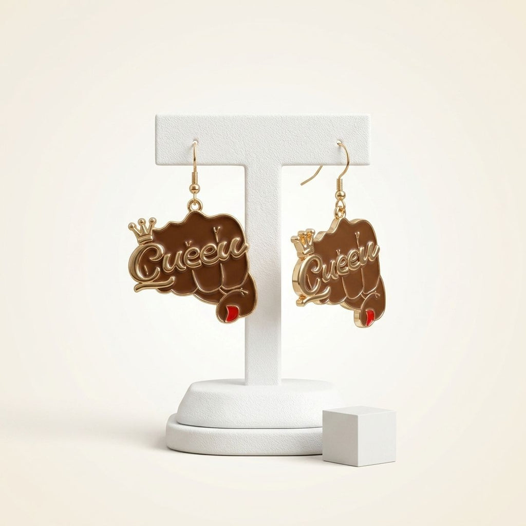 Pair of brown epoxy raised fist "Queen" crown gold fish hook dangle earrings hanging on white T-bar earring display stand on cream background, showing full charm detail with red nail accent and gold crown