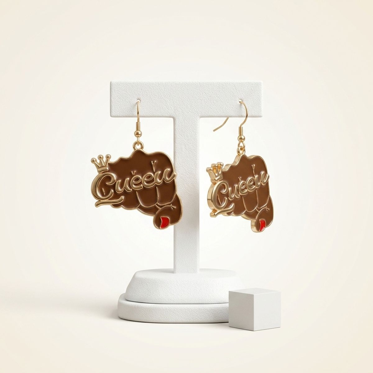 Pair of brown epoxy raised fist "Queen" crown gold fish hook dangle earrings hanging on white T-bar earring display stand on cream background, showing full charm detail with red nail accent and gold crown