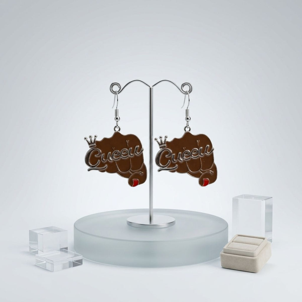 Pair of brown epoxy raised fist "Queen" crown fish hook dangle earrings hanging on silver double-hook earring display stand on frosted glass base, with clear acrylic blocks and cream velvet ring holder in background