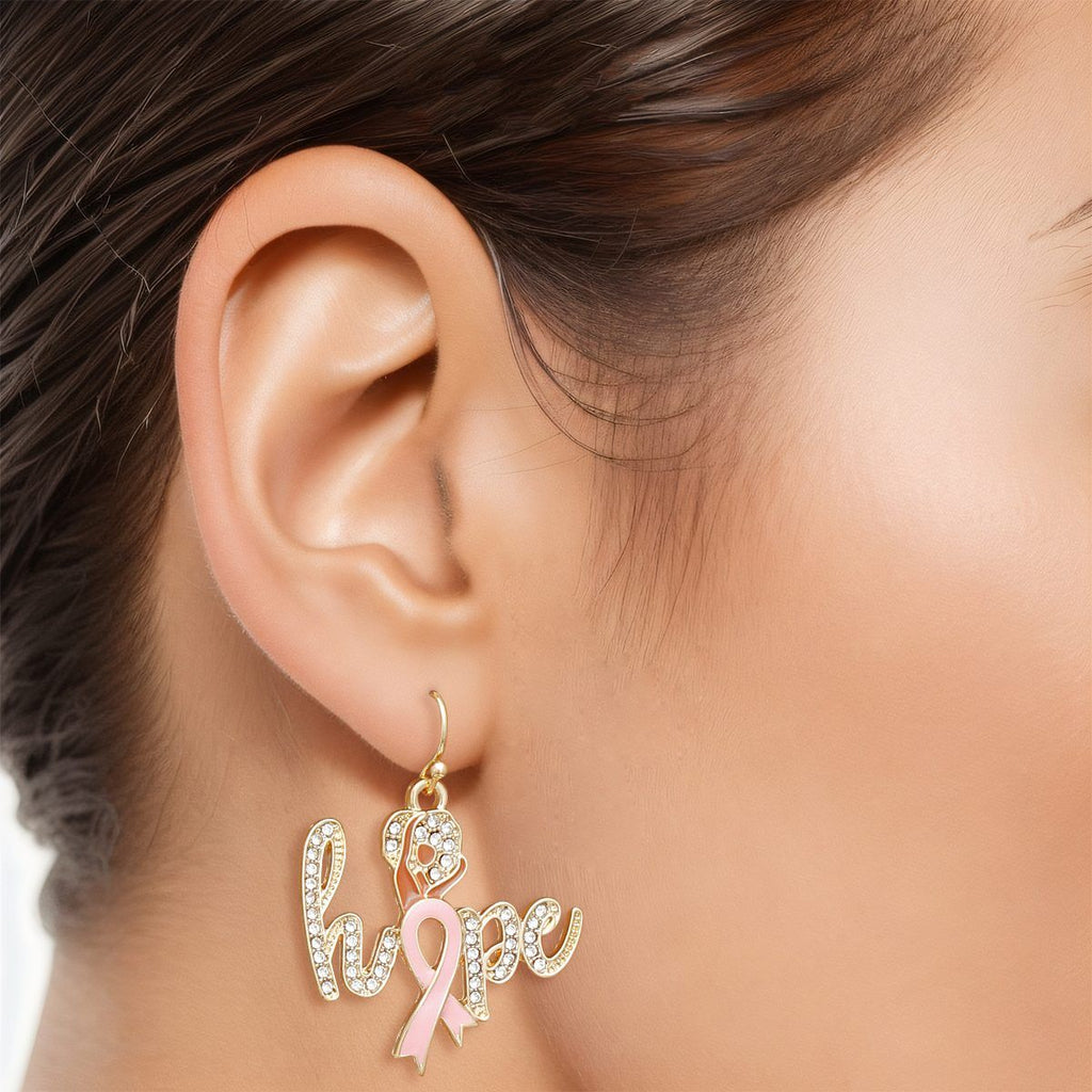Woman wearing a breast cancer awareness gold rhinestone hope dangle earring with Afro woman silhouette and light pink enamel ribbon on a fish hook