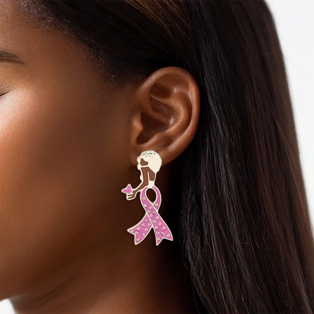 Woman wearing a breast cancer awareness gold stud earring shaped like a woman with a short Afro, pink rhinestone ribbon body and pink butterfly in her hand