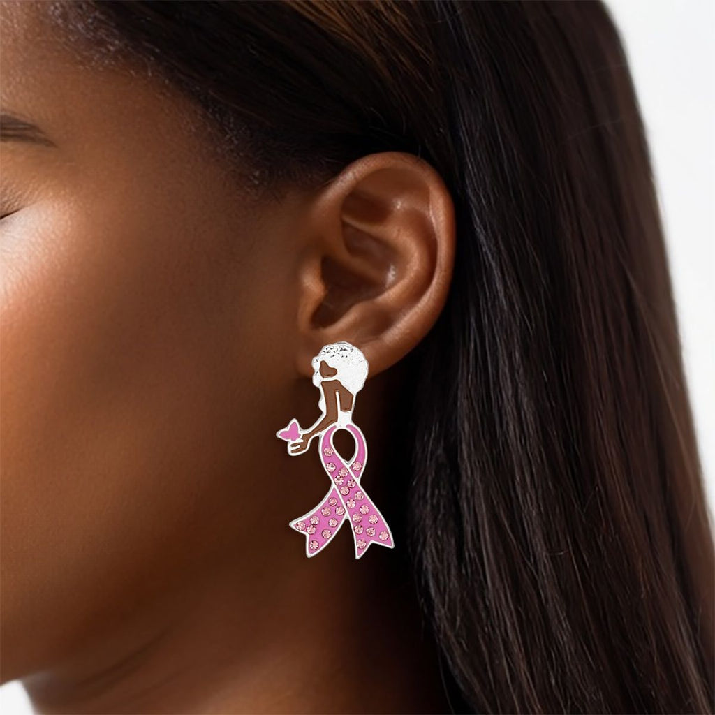 Woman wearing a breast cancer awareness silver stud earring shaped like a woman with a short Afro, pink rhinestone ribbon body and pink butterfly in her hand