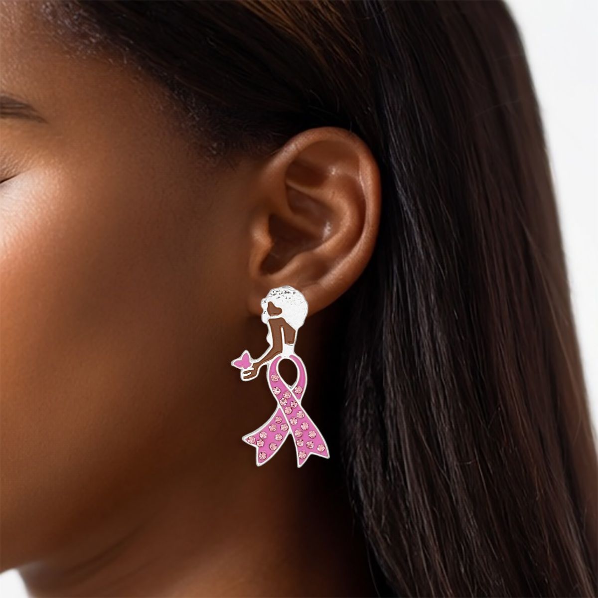Woman wearing a breast cancer awareness silver stud earring shaped like a woman with a short Afro, pink rhinestone ribbon body and pink butterfly in her hand