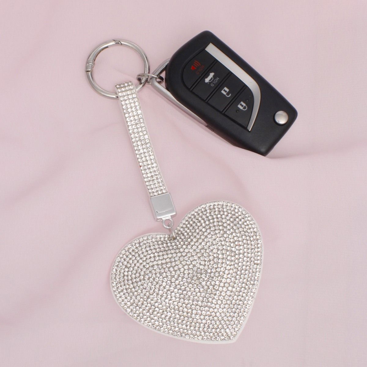 Full rhinestone-covered white padded heart bag charm keychain with multi-row crystal strap, shown attached to a car key fob with silver split keyring on pink background