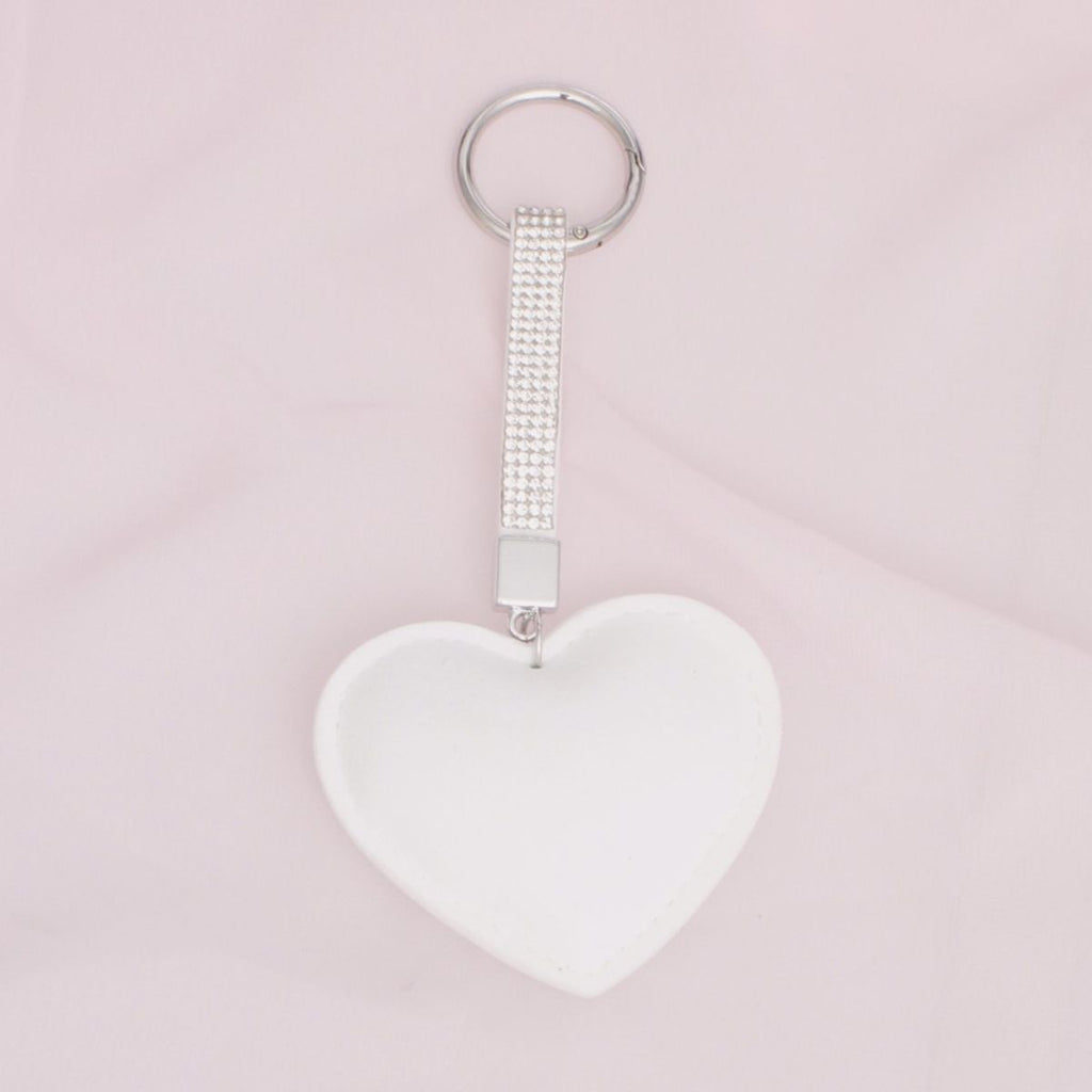 White padded heart bag charm keychain with rhinestone-encrusted strap and silver rhodium ring clip on pink background