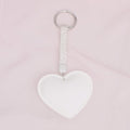 White padded heart bag charm keychain with rhinestone-encrusted strap and silver rhodium ring clip on pink background