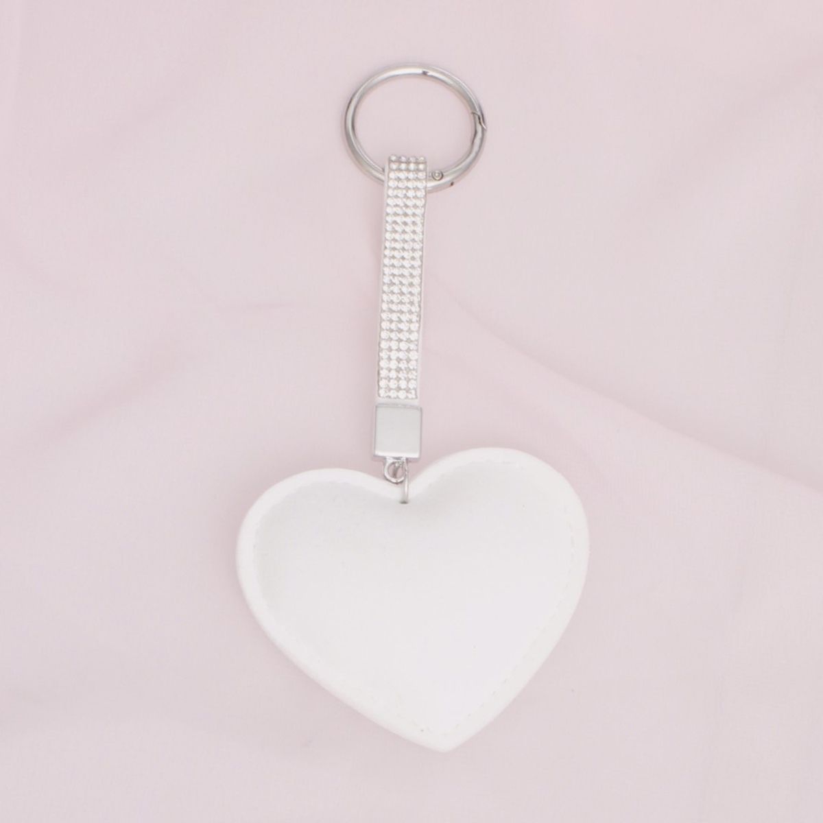 White padded heart bag charm keychain with rhinestone-encrusted strap and silver rhodium ring clip on pink background