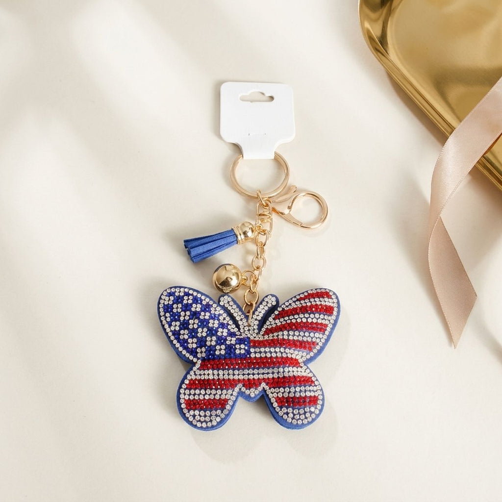 Patriotic butterfly rhinestone keychain with American flag detail, blue tassel, and gold lobster clasp on white surface with retail tag