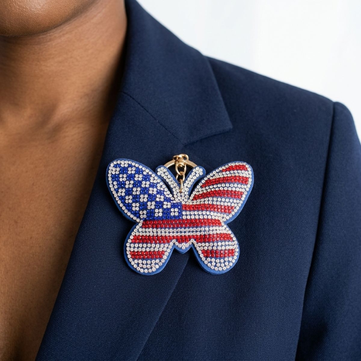 Close-up of American flag rhinestone butterfly charm clipped to navy blue blazer lapel, showing red, white, and blue crystal detail