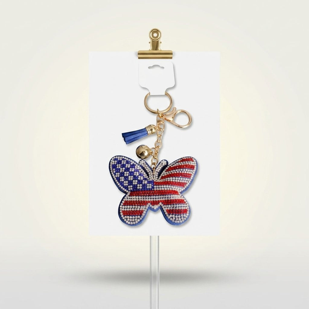 Patriotic butterfly bag clip keychain with American flag rhinestone detail, blue mini tassel, and gold lobster clasp on white display card
