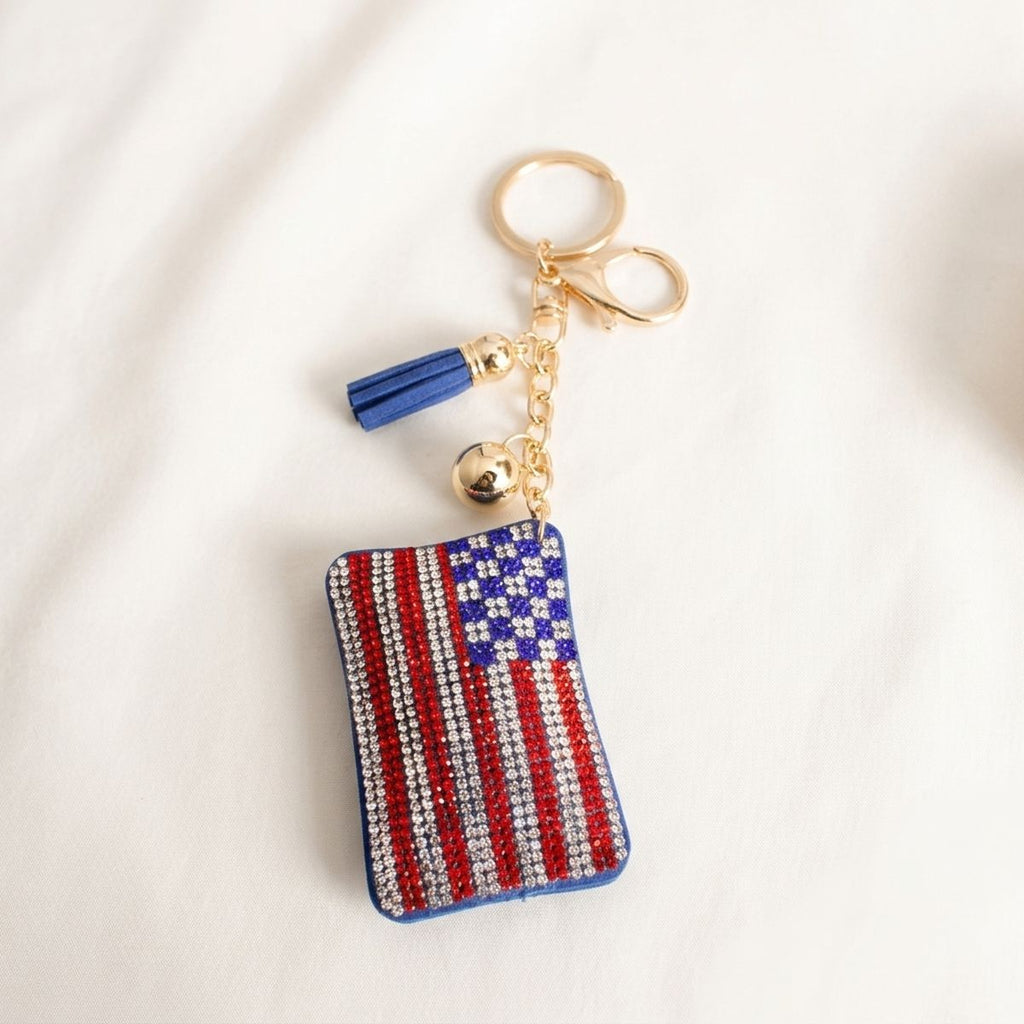 Patriotic American flag rhinestone keychain with blue tassel and gold hardware on white fabric background