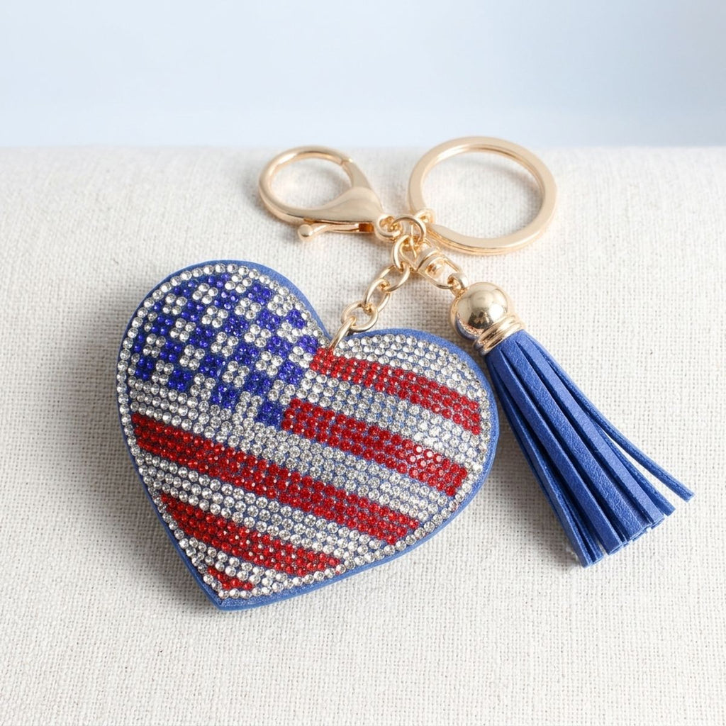 American flag rhinestone heart keychain with blue faux leather tassel and gold lobster clasp, flat lay on linen surface