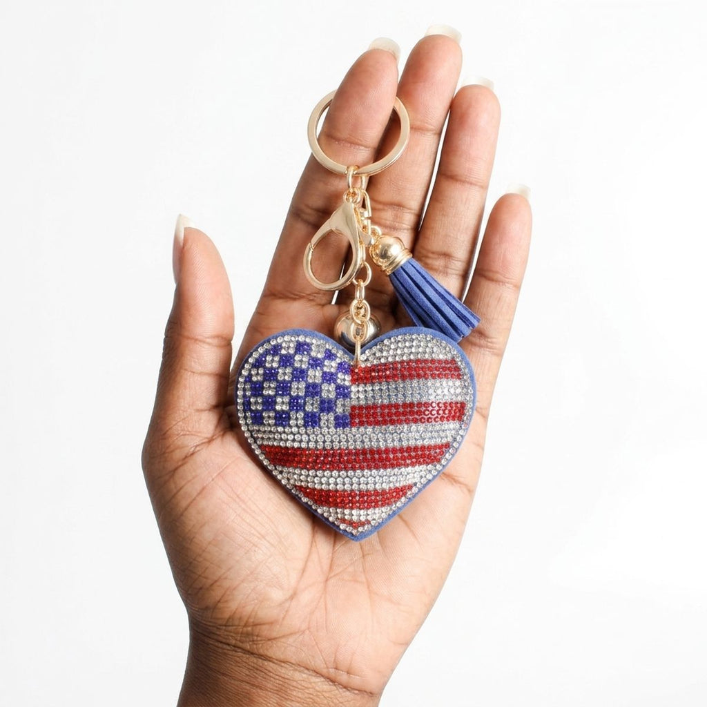 American flag rhinestone heart bag charm keychain held in hand, showing red, white, and blue crystal detail with blue tassel and gold hardware