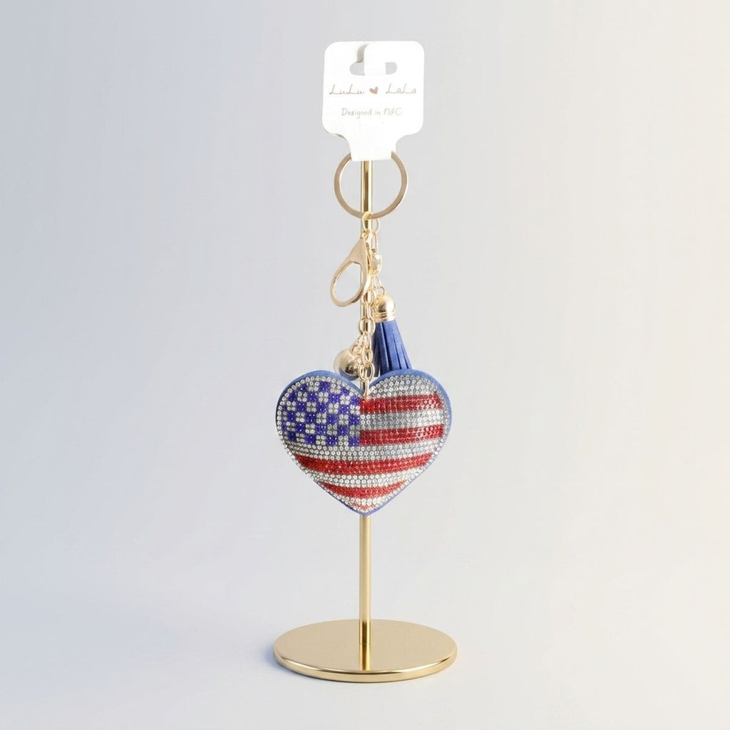 Patriotic heart rhinestone keychain with American flag detail and blue tassel displayed on gold retail stand with hang tag