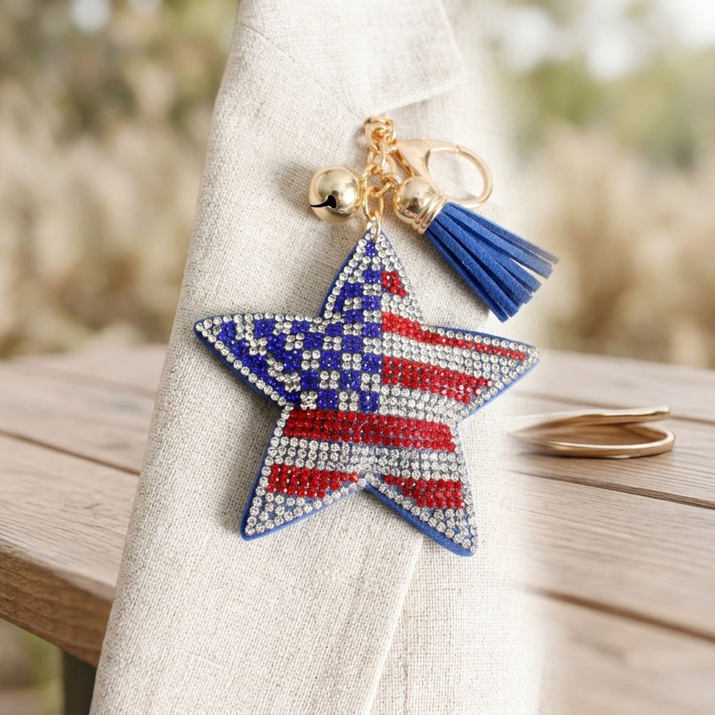 Patriotic star rhinestone bag charm keychain with blue tassel and gold lobster clasp, styled on linen fabric