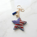 Patriotic star rhinestone keychain with American flag detail, blue tassel, and gold hardware on marble surface