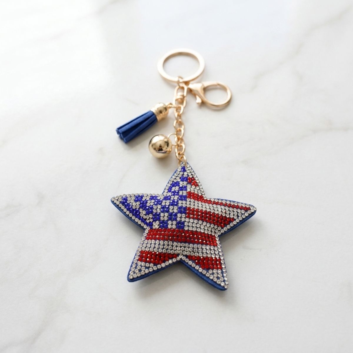 Patriotic star rhinestone keychain with American flag detail, blue tassel, and gold hardware on marble surface