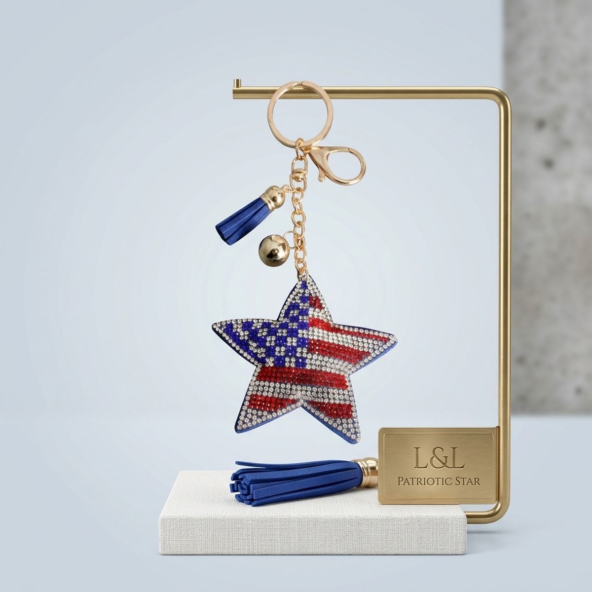 Patriotic star rhinestone bag charm keychain with blue tassel displayed on gold jewelry stand