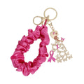Hot pink satin scrunchie wristlet keychain looped open beside a gold-tone lady charm with clear rhinestone butterfly gown, pink enamel butterfly and pink awareness ribbon